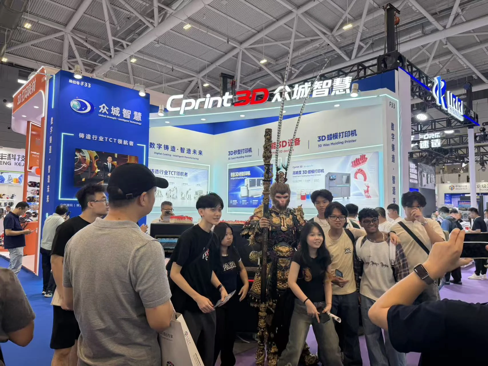 Visitantes posam com o intérprete de Black Myth: Wukong em frente ao estande da Cprint3D