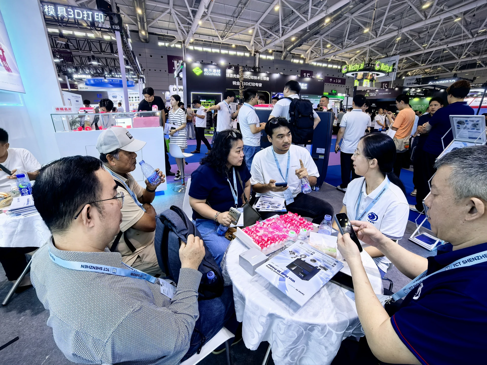 A equipe da Cprint3D conversa com visitantes em uma mesa com amostras de cera e materiais de produto
