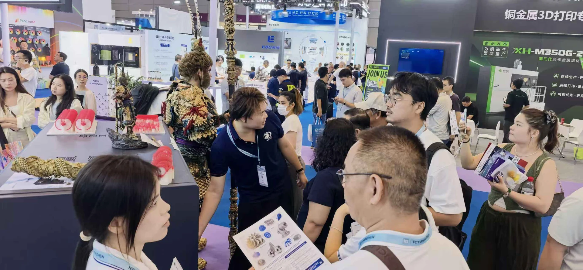 A equipe da Cprint3D conversa com visitantes que seguram materiais de produto perto das criações de Black Myth: Wukong e das amostras de cera