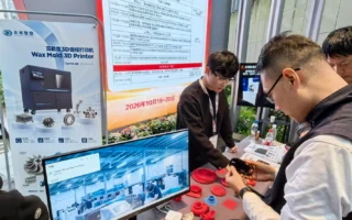 Besucher betrachten ein Muster neben einem Cprint 3D Wachs-Druckeraufsteller und roten Wachsmodellen auf der Feingusskonferenz