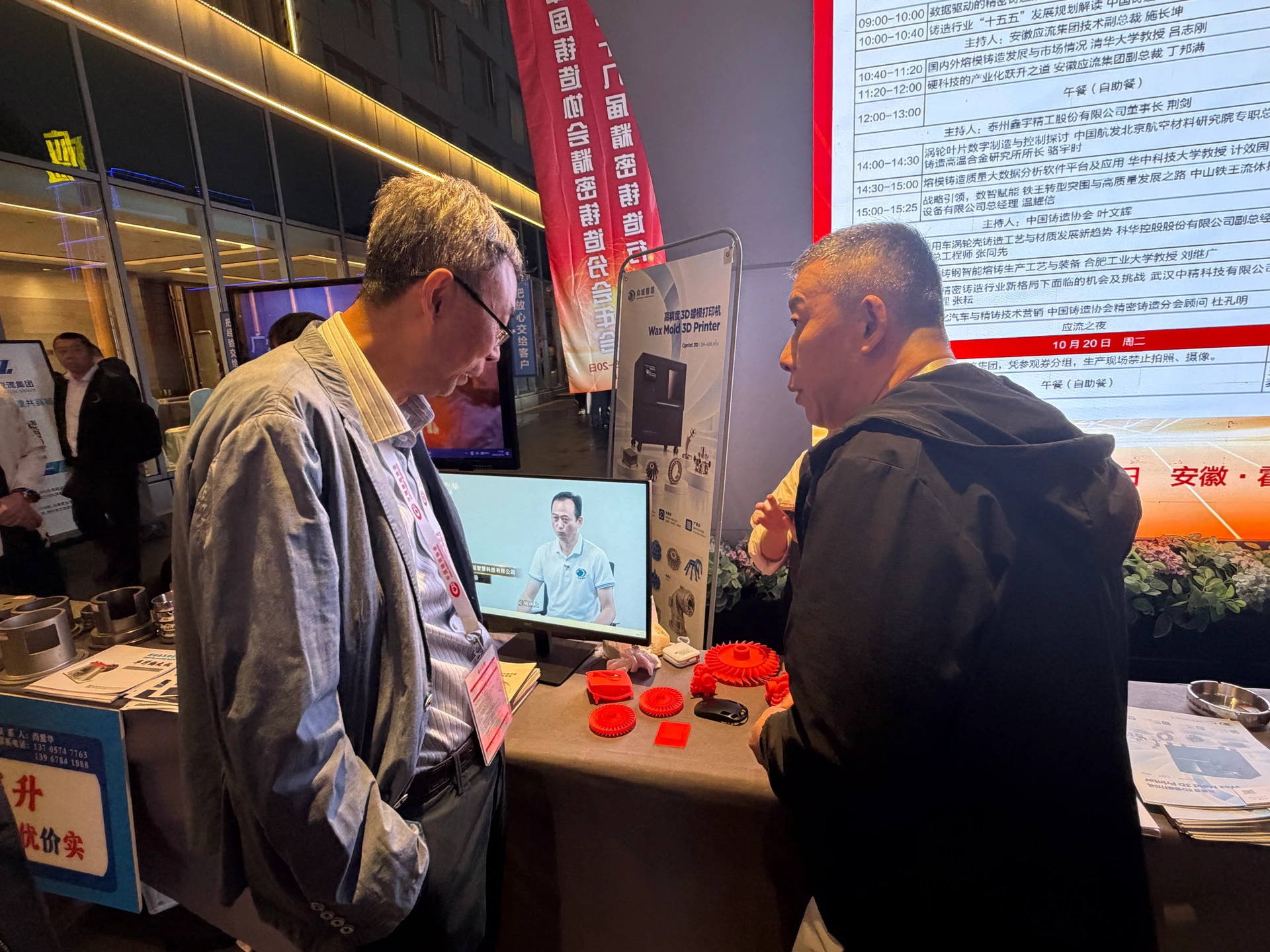 Konferenzteilnehmer im Gespräch am Stand von Cprint 3D mit roten Laufrad-Wachsmodellen auf dem Tisch und einem Druckeraufsteller im Hintergrund