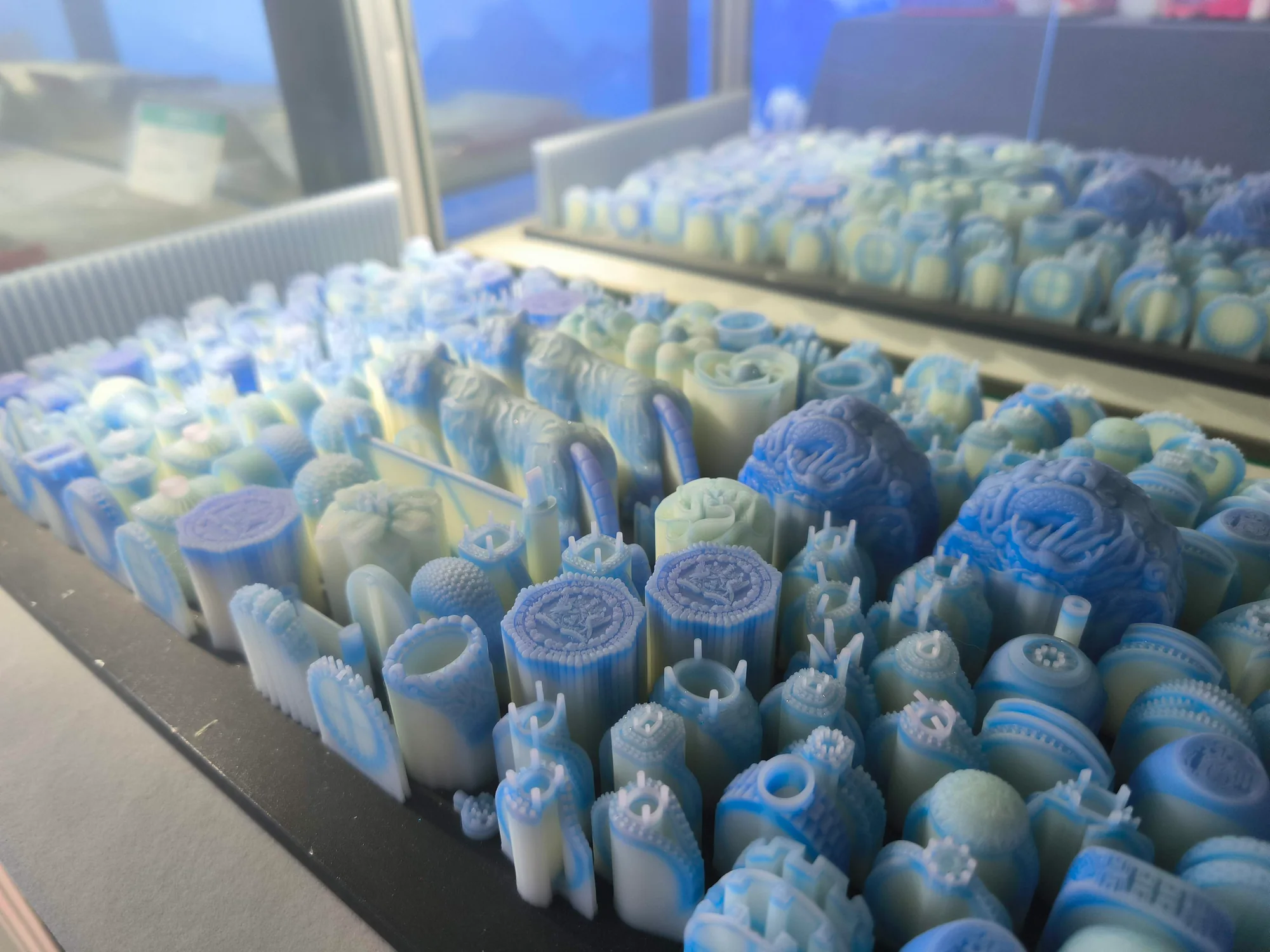 Multiple blue jewelry patterns with light-colored support structures arranged closely on printing platforms