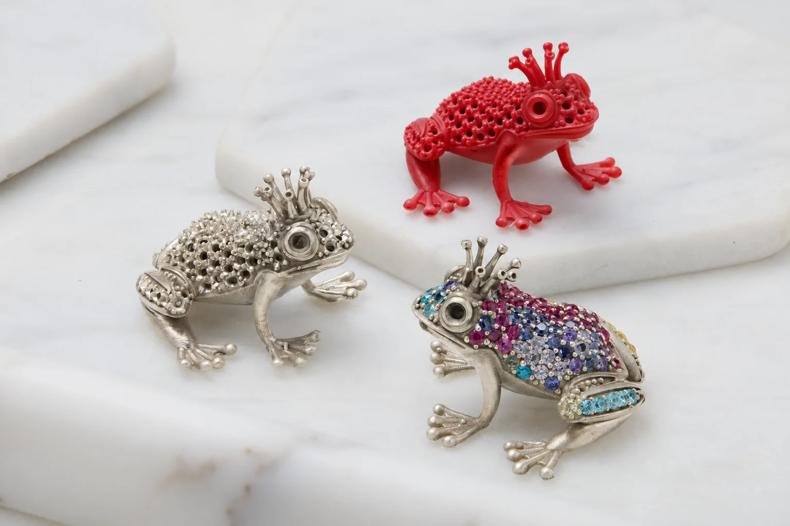Frog forms illustrating a red pattern, a silver-colored metal appearance and a colorful stone-set appearance